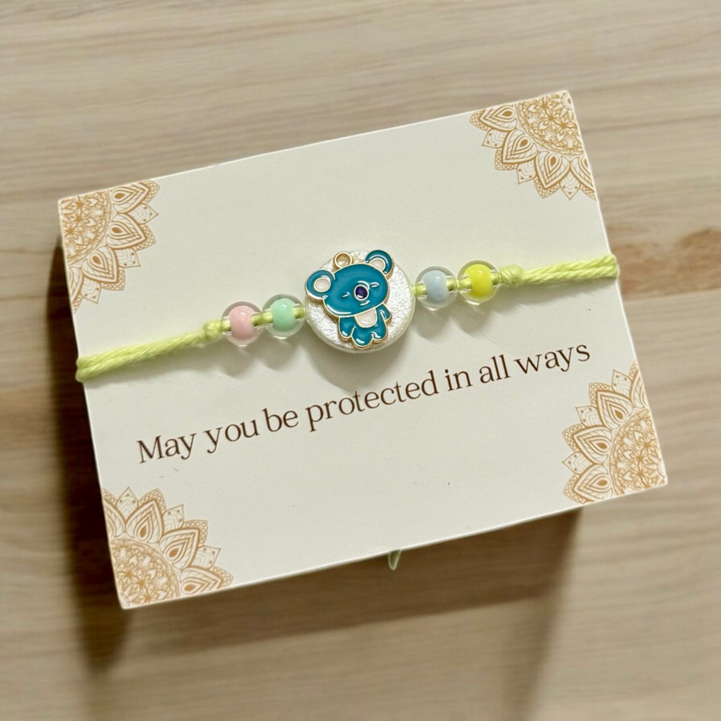 Bracelet with a teddy bear charm on a decorative card with text, on a wooden surface.