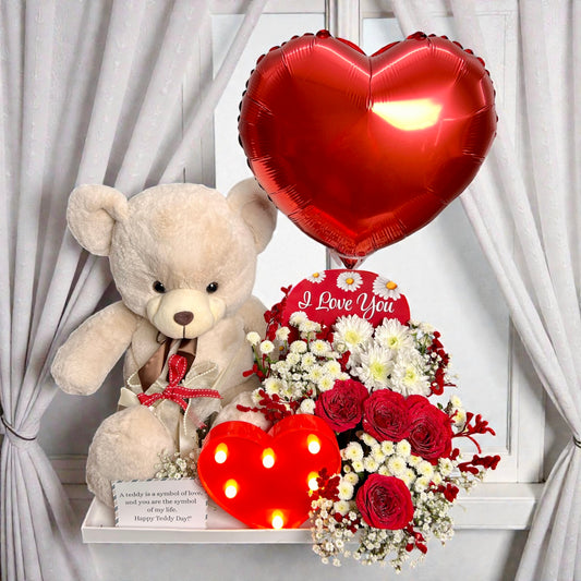 Valentine's Day arrangement with teddy bear, heart-shaped balloon, and flowers on a white background.