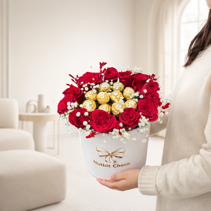 Person holding a bouquet of red roses and gold chocolate balls in a white box with 'Nutbit Choco' branding.