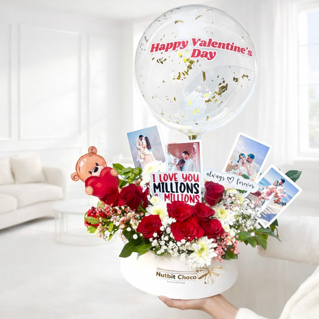 Valentine's Day arrangement with flowers, balloon, and photos on a white surface.