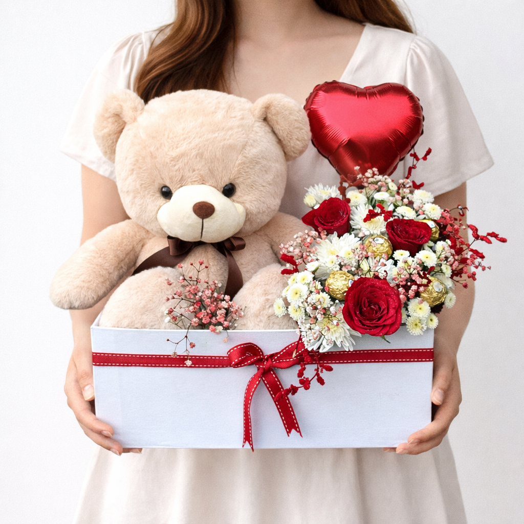 Person holding a gift box with a teddy bear, flowers, and a heart-shaped balloon.