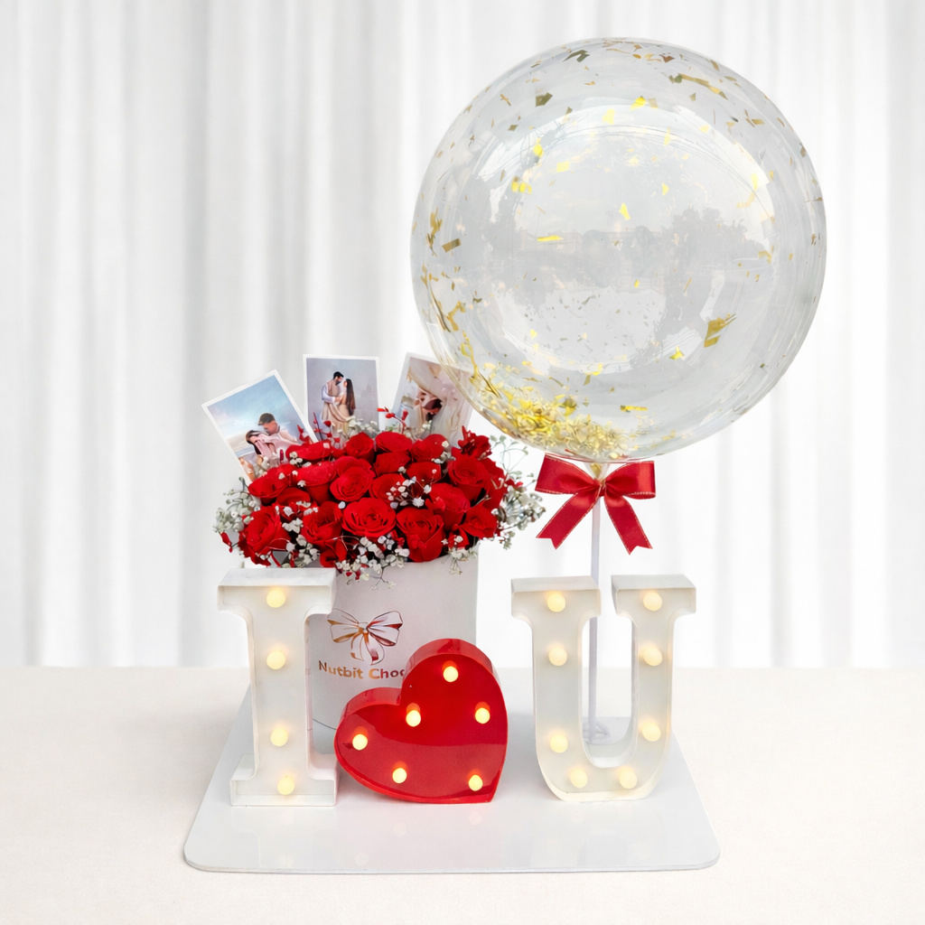 Decorative setup with red roses, a transparent balloon with gold confetti, and a heart-shaped light on a white background.
