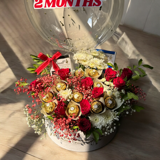 Floral arrangement with chocolates and a clock showing '2 Months' in the background.