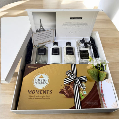 Gift set with Ferrero Rocher chocolates, skincare products, and a card on a wooden surface.