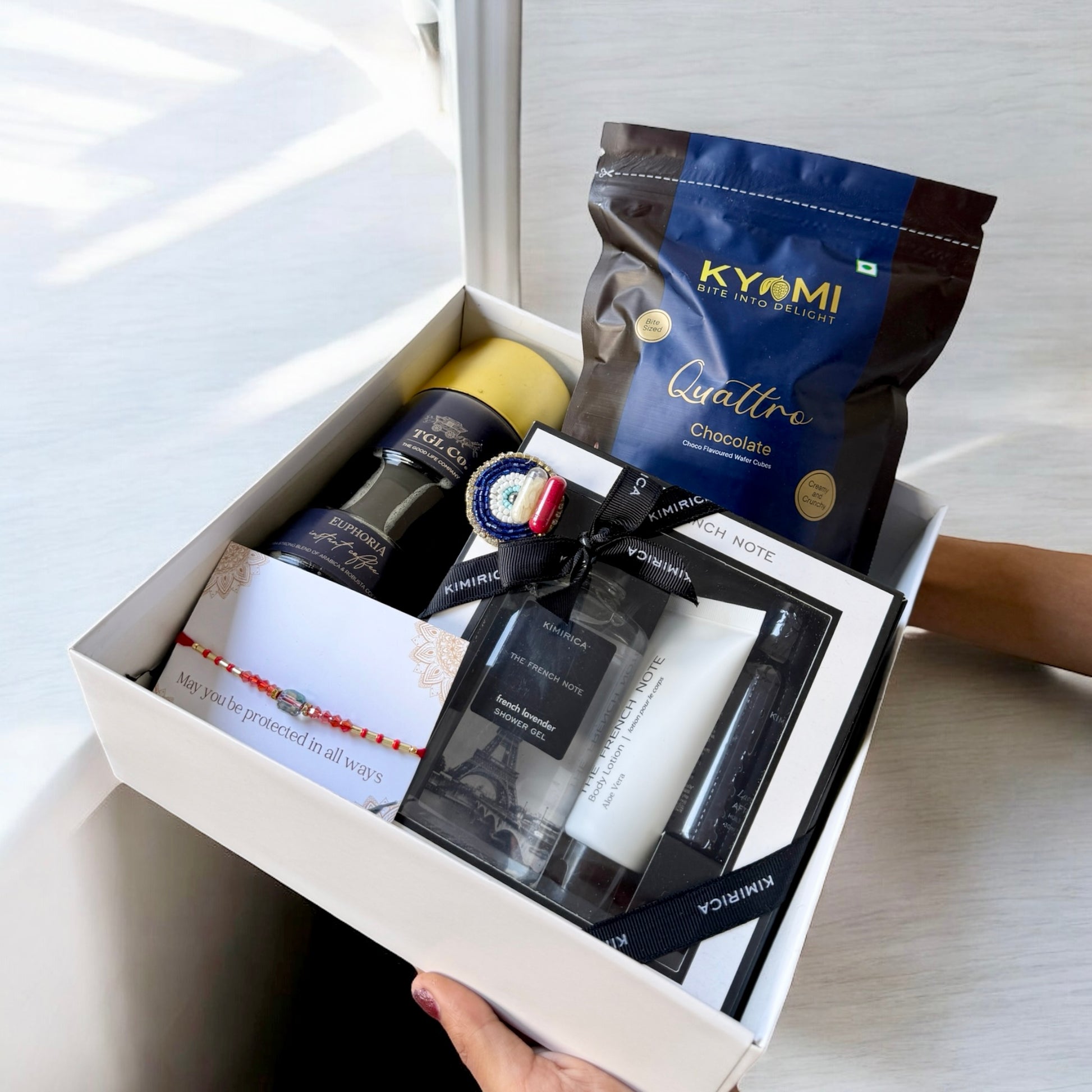 Gift box with skincare products and a chocolate bag on a light background