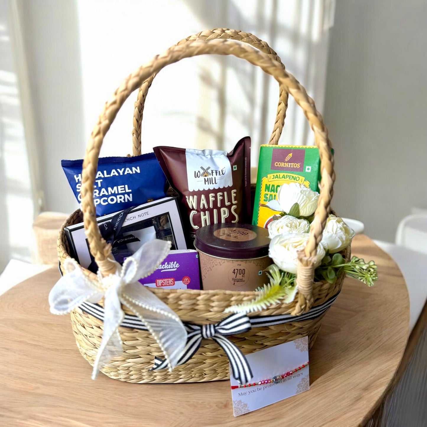 Gift basket with snacks, coffee, and flowers on a wooden table.