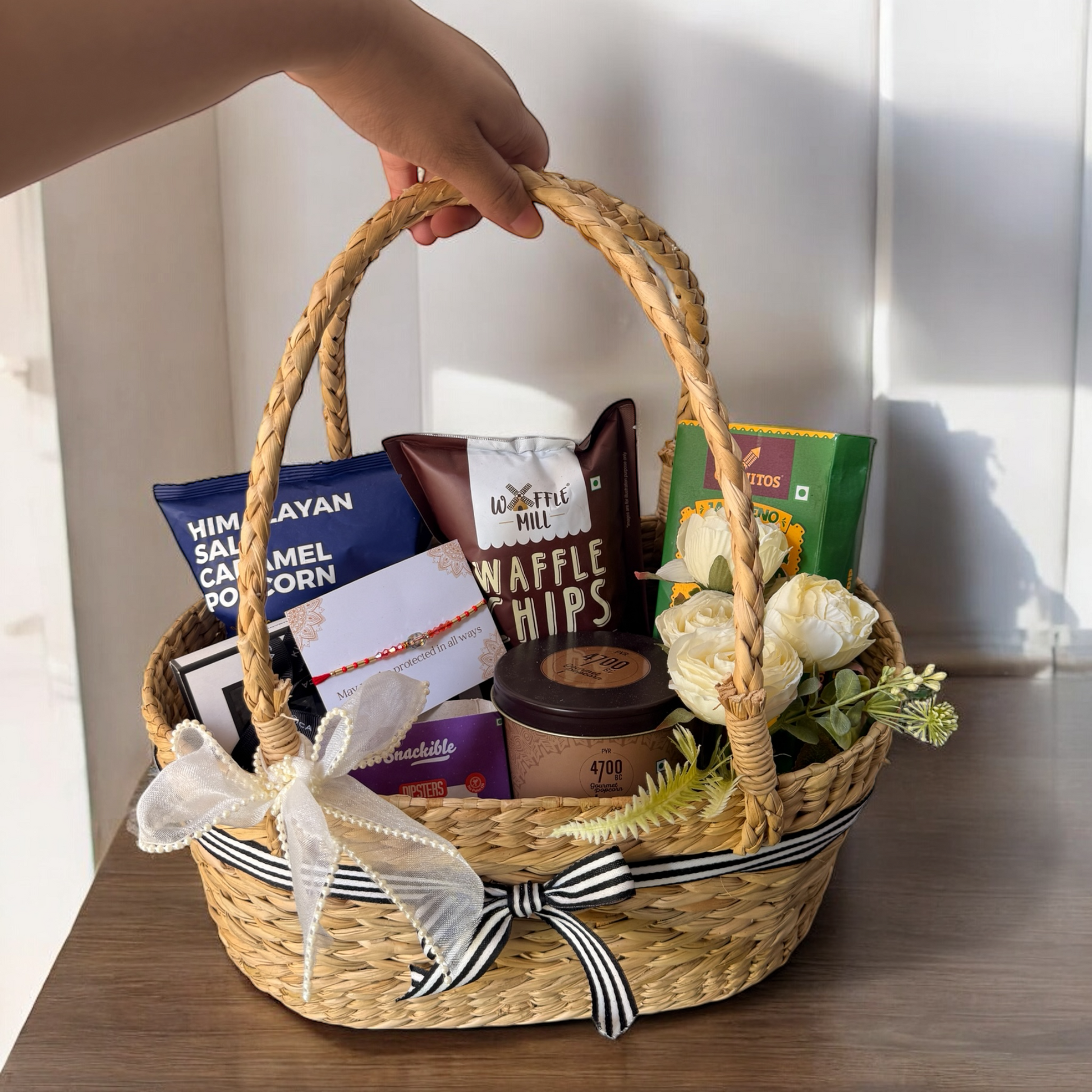 Woven gift basket with snacks and flowers on a wooden surface