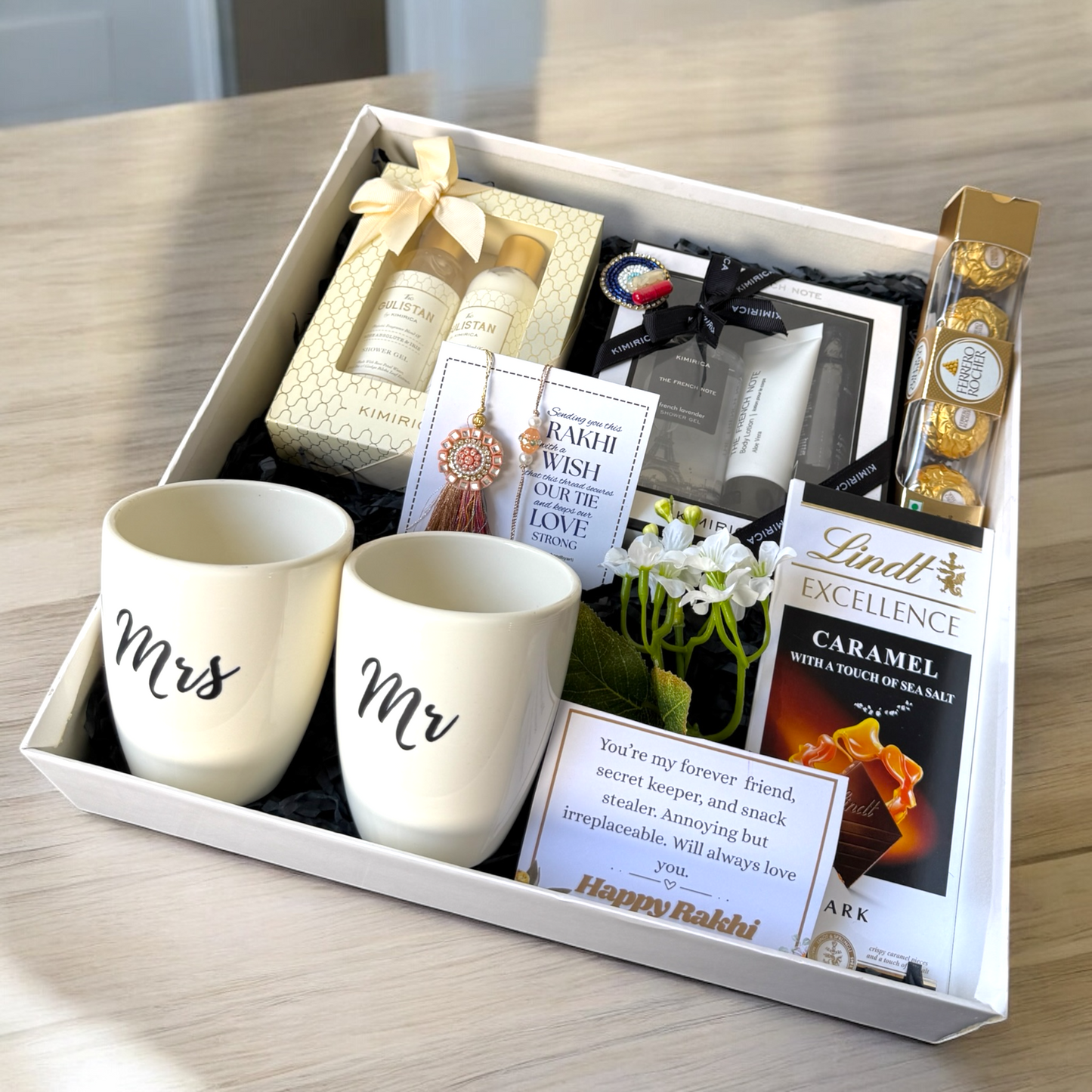 Gift set with 'Mr' and 'Mrs' mugs, Lindt chocolate, and other items in a box on a wooden surface.