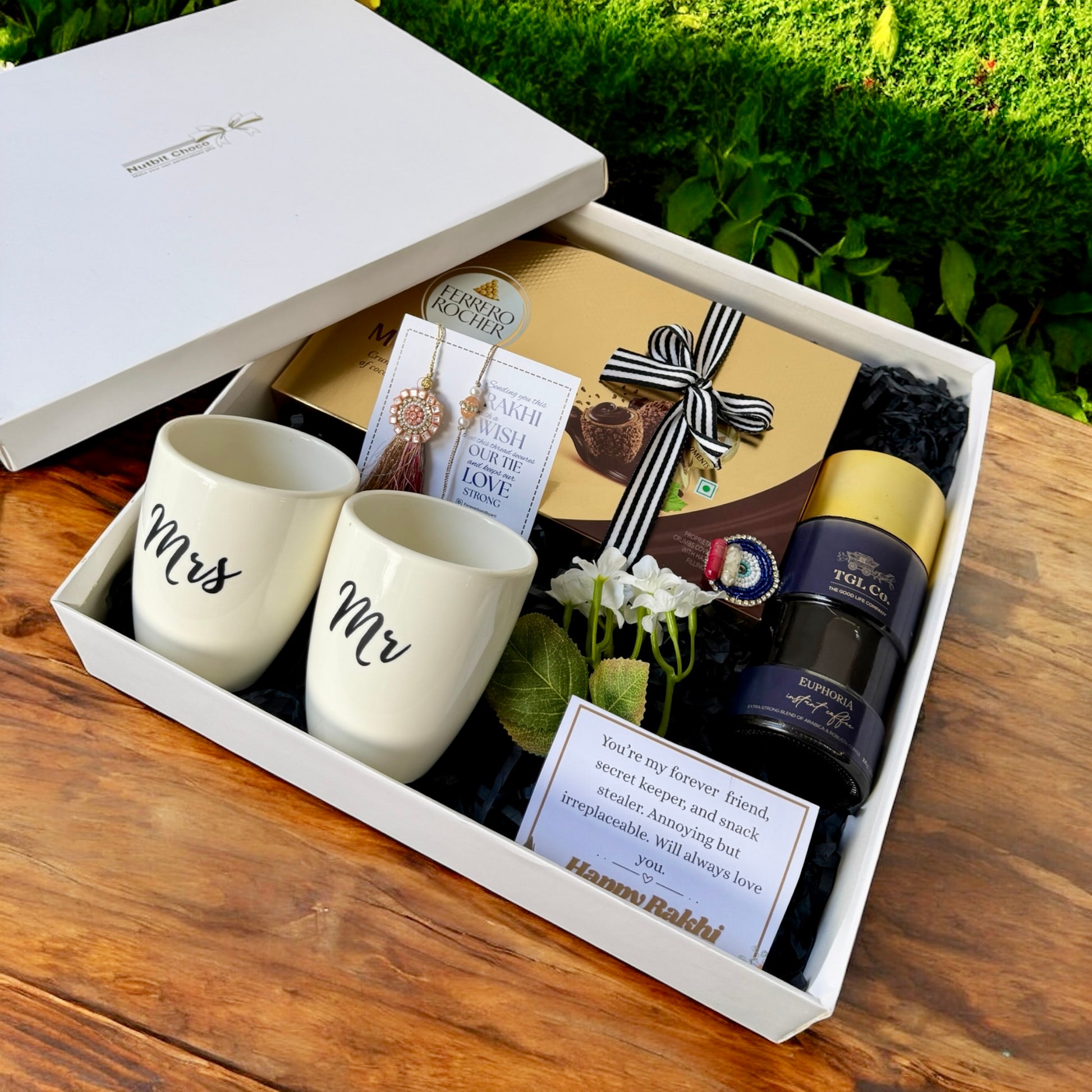 Gift set with 'Mr' and 'Mrs' mugs, a bottle of wine, and other items in a box on a wooden surface.