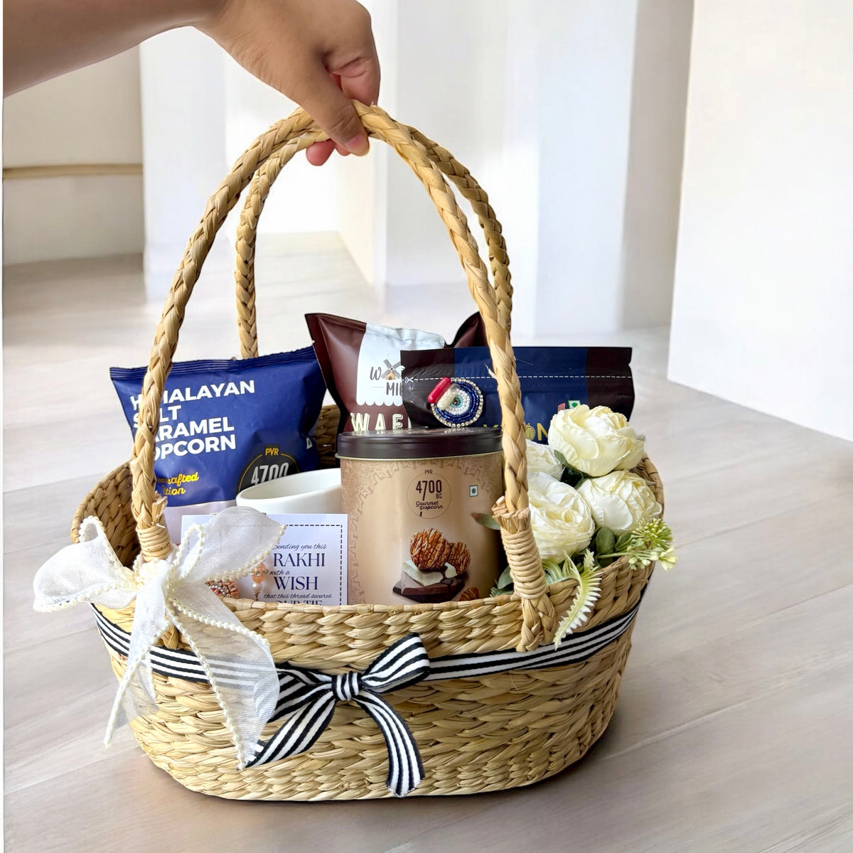 Gift basket with snacks and flowers on a light wooden surface