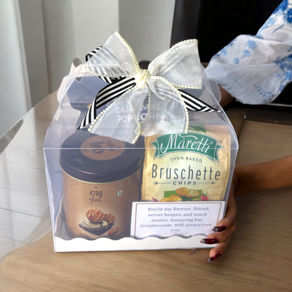 Gift set with Maretti Bruschette Chips and a coffee can in a clear box with a bow, held by a person.