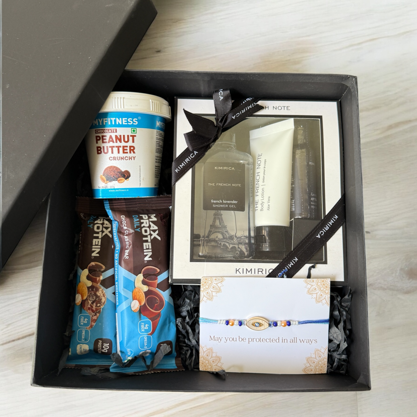 Gift box with peanut butter, protein bars, and other items on a wooden surface