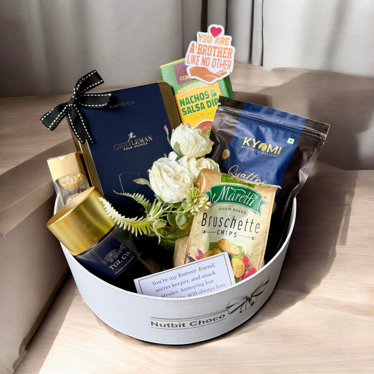Gift basket with snacks, flowers, and a bottle on a wooden surface
