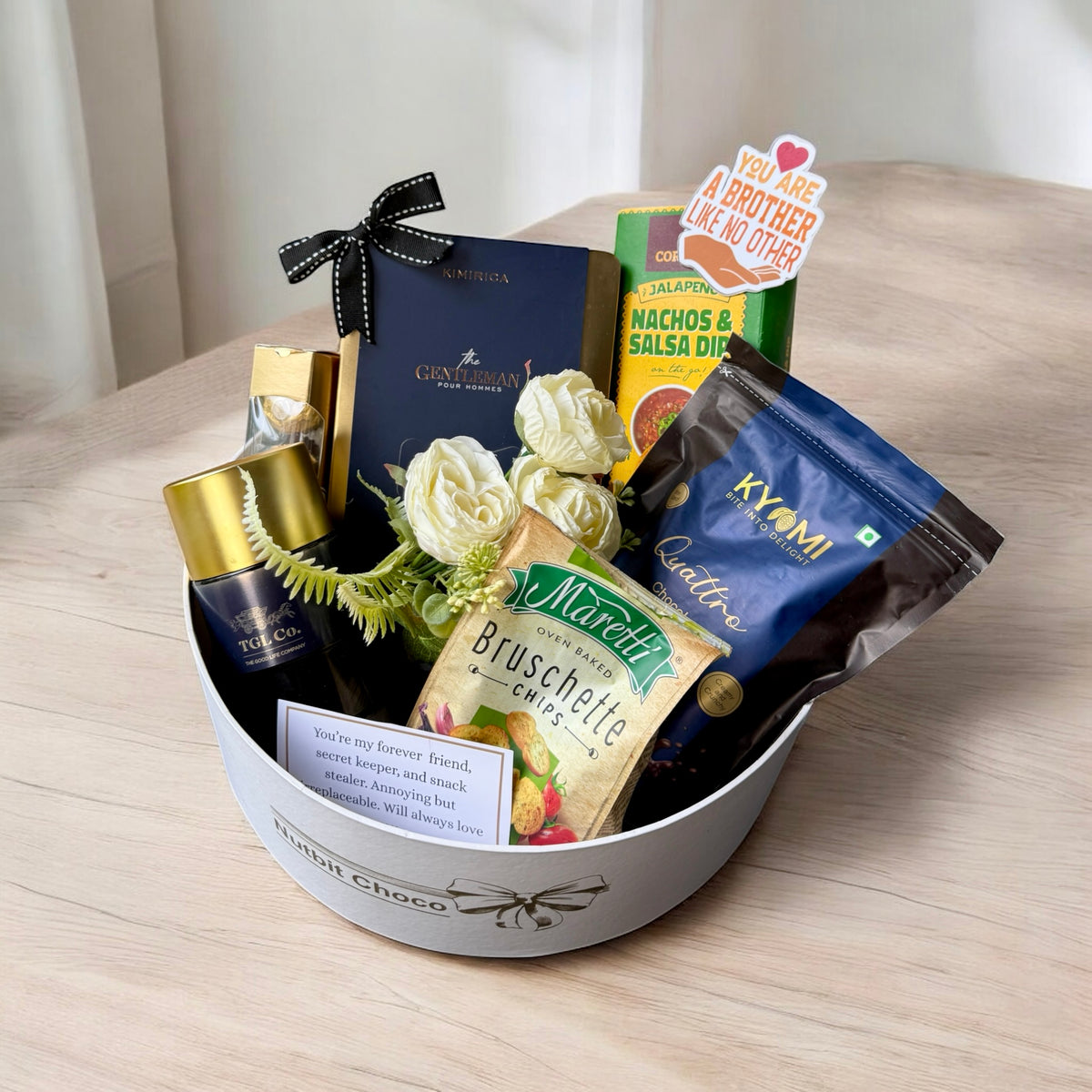 Gift basket with snacks, flowers, and a bottle on a wooden surface