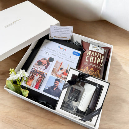 Gift box with electronic device, snacks, and other items on a wooden surface