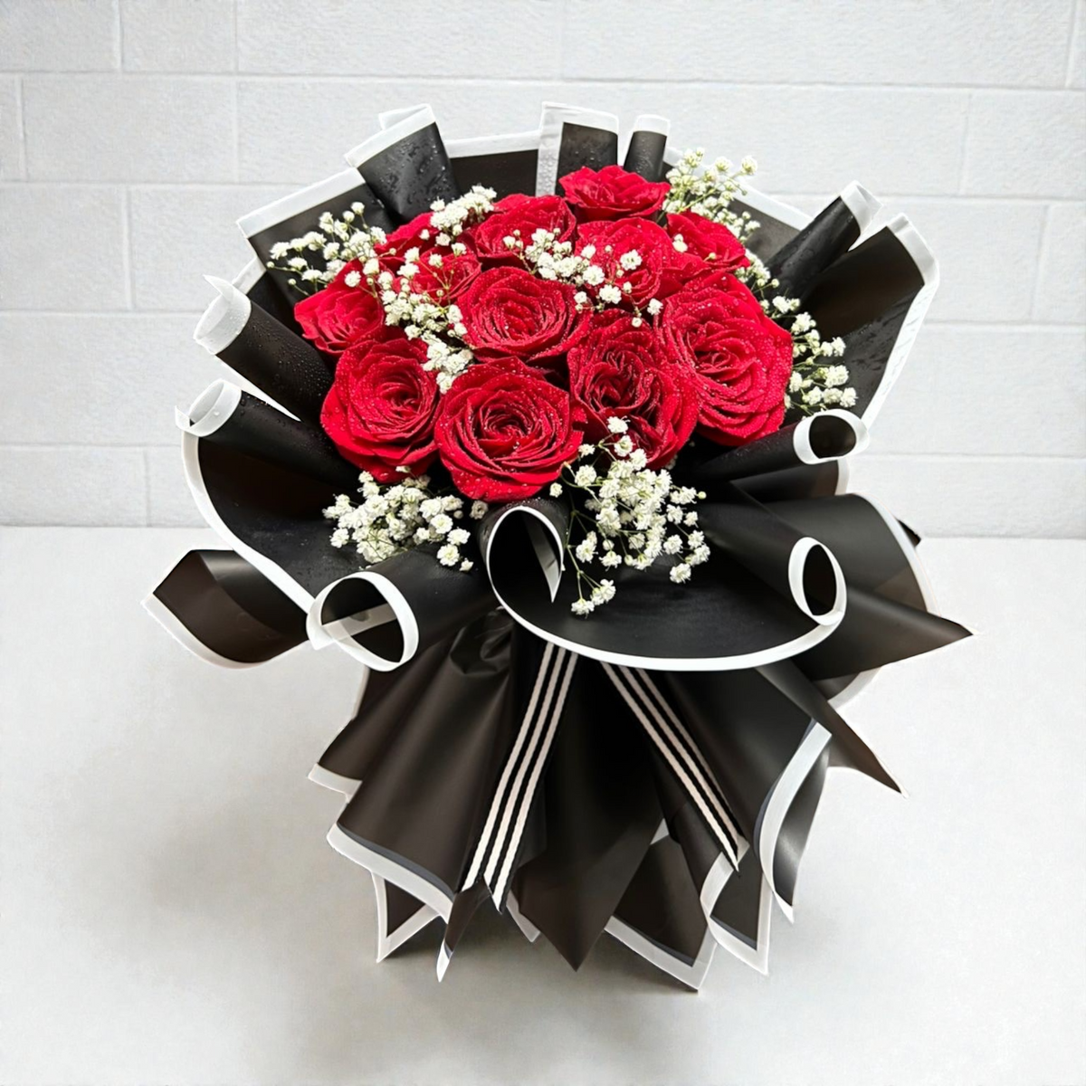 Bouquet of red roses with black and white ribbons on a light gray background