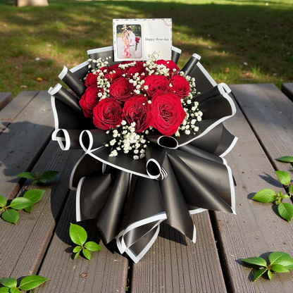 Bouquet of red roses wrapped in black paper on a wooden surface with greenery.
