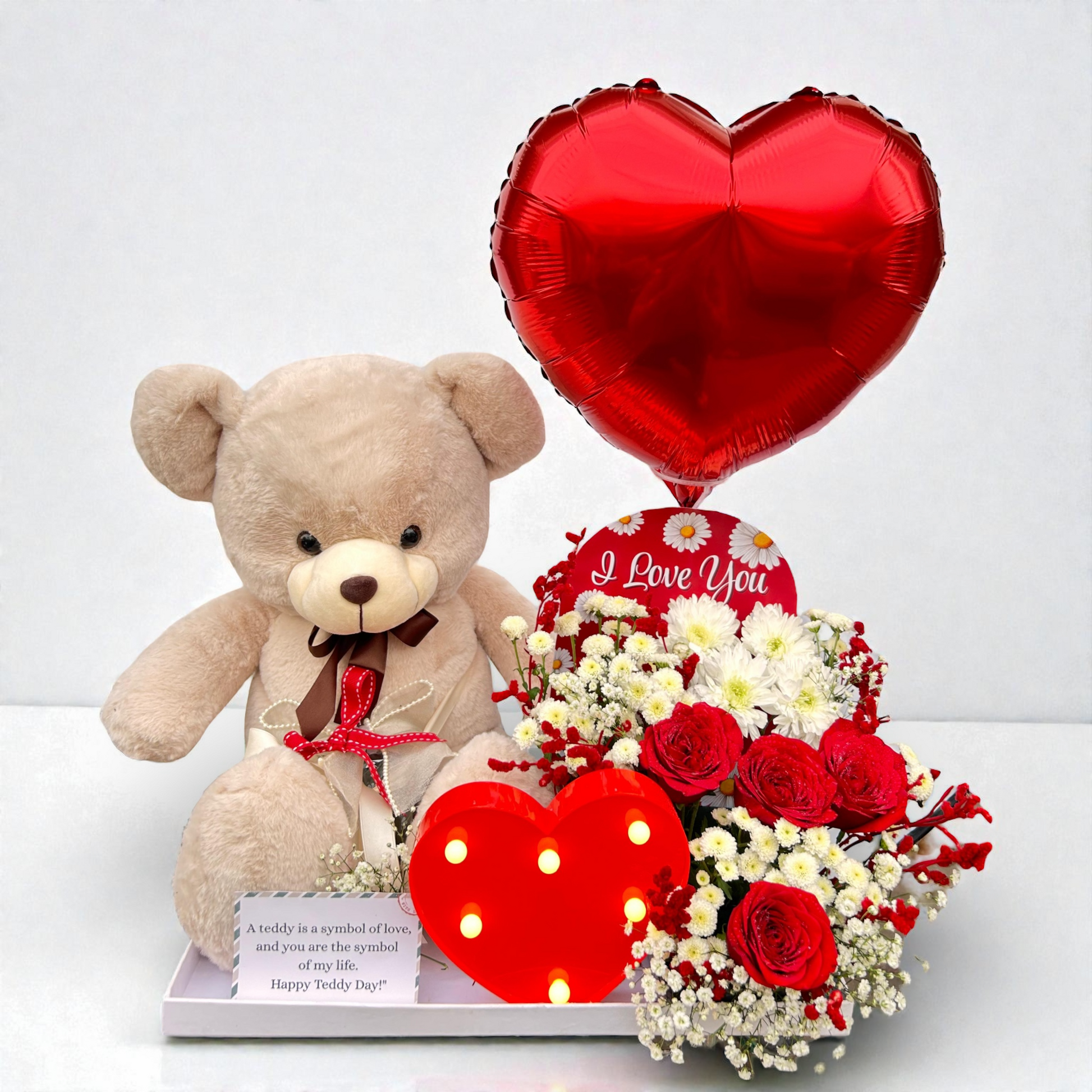 Teddy bear with red heart balloon, flowers, and 'I Love You' card on a white background