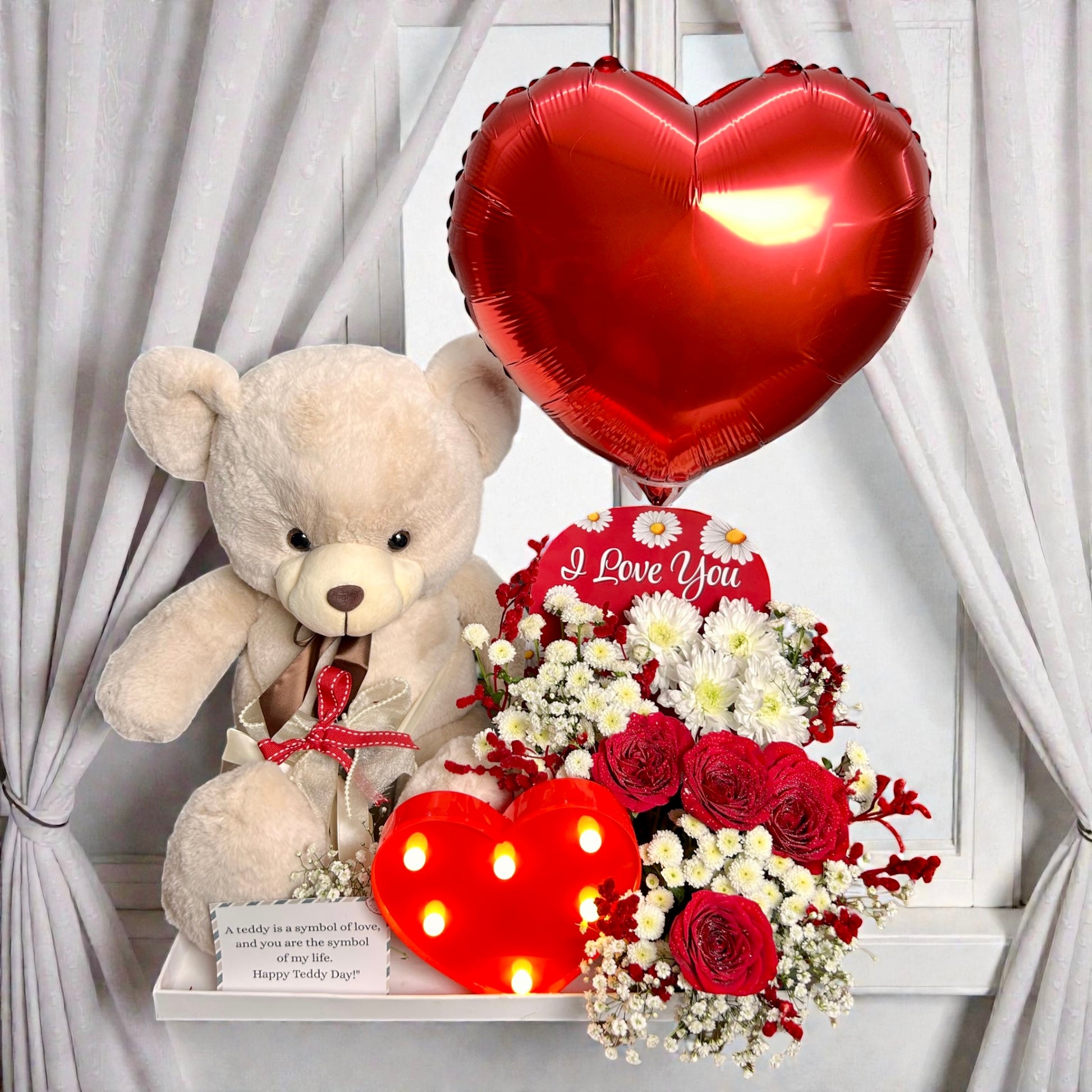 Valentine's Day arrangement with teddy bear, heart-shaped balloon, and flowers on a white background.