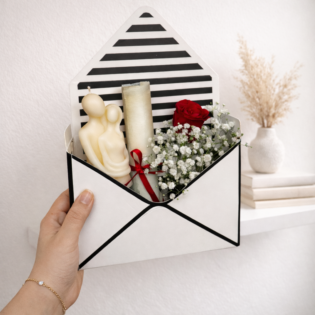 Hand holding a geometric black and white striped box with candles and flowers on a light background